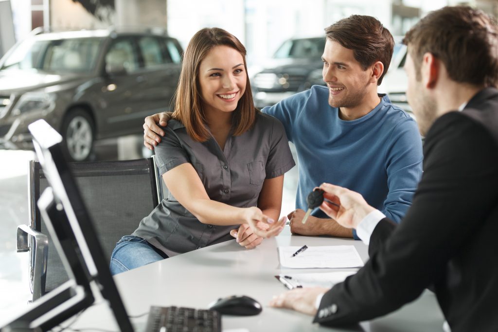 Affordable-Car salesman giving the key of the new car to the young attractive owners – her dreams come true