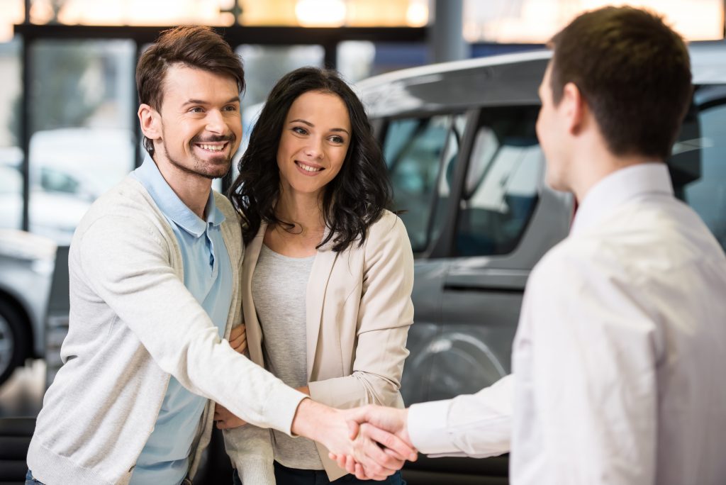 Young couple grateful sales manager for advice in auto salon